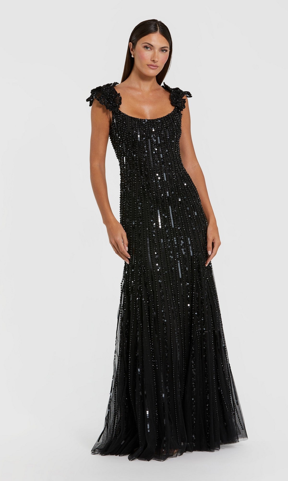 A woman stands in the Mac Duggal 94223 long formal dress, a floor-length, sleeveless black gown featuring mesh fabric with sequins and textured shoulder details, set against a plain white background.